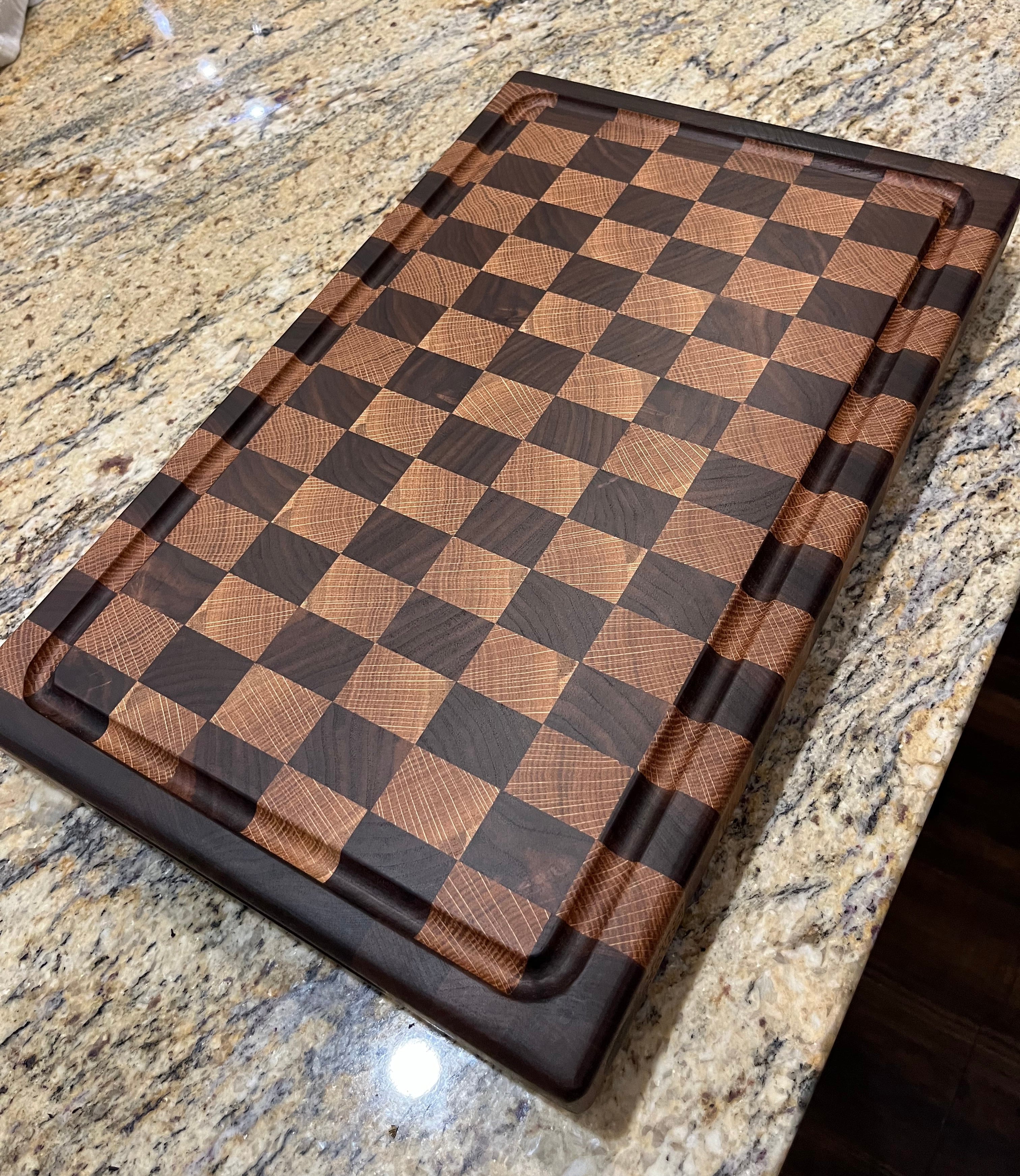 A rectangular wooden cutting board with a checkered pattern of light and dark brown wood squares, shown resting on a speckled granite countertop.